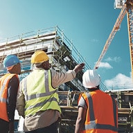 Construction workers in safety gear observing a building site with a crane